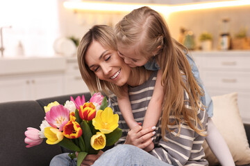 Wall Mural - Little daughter congratulating her mom with Mother`s Day at home. Woman holding bouquet of beautiful tulips