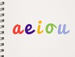 Colorful handwritten AEIOU lowercase vowels on a notebook