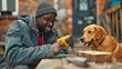 A inquisitive dog watches as a black guy drills into a piece of wood while carrying a drill in his right hand.