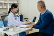 © ArLawKa - Asian professional female doctor talking with male patient about his pain and symptoms while giving consultation at table in examination room at health care hospital