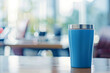 Blue insulated tumbler on wooden table in bright office with natural light