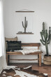 Minimalist Western style wooden bench with cactus, white wall, black and brown cowhide rug, boho pillows, cacti in the background, hanging canvas art in the style of on simple wood frame.