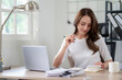 © Wasana - Confident female entrepreneur calculates and analyzes documents while working from home office.