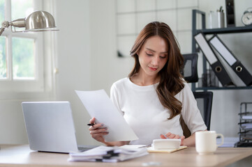 Confident female entrepreneur calculates and analyzes documents while working from home office.