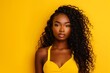 Radiant beauty against yellow background: confident young woman poses with striking curly hair on a vibrant yellow backdrop