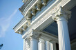 A close-up of the ornamental pediments and cornices of an Italianate porch, showcasing the house against a sky blue backdrop