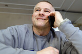 Fototapeta Do przedpokoju - A cheerful man is captured enjoying a conversation on a mobile phone. The sincere smile on his face reflects the positive nature of the conversation