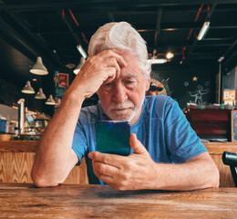 Sticker - Serious bearded senior white-haired man sitting at cafe table using mobile phone reading unpleasant news