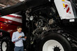 © scharfsinn86 - Serviceman with digital tablet on a next to ombine harvester with open hood..