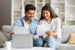 © Prostock-studio - Smiling hindu couple reviewing documents with laptop at home