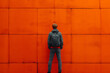 The man stands facing a bright orange wall.