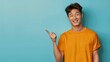 Happy young man in yellow t-shirt pointing to copy space on a blue background. Advertisement concept