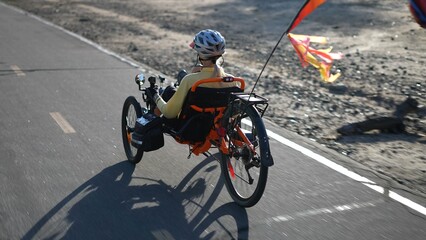 Rear side view of elderly senior woman riding a recumbent electric bike on a bike path in Southern California. Filmed in.