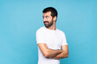 © luismolinero - Young man with beard  over isolated blue background with arms crossed and happy