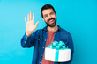 Young handsome man with a big cake over isolated blue background saluting with hand with happy expression
