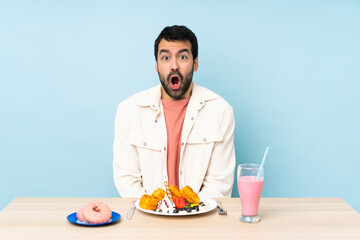 Wall Mural - Man at a table having breakfast waffles and a milkshake with surprise facial expression