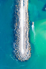 Fototapete - a fishing boat entering a harbor protected by a breakwater, turquoise water. Drone photography