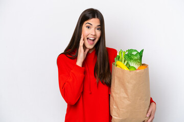 Wall Mural - Young Brazilian woman holding a grocery shopping bag isolated on white background with surprise and shocked facial expression