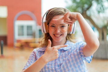 Wall Mural - Young redhead girl headphones at outdoors focusing face. Framing symbol