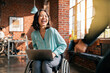 An Asian woman in a wheelchair laughs heartily in a modern office setting, signifying inclusion and happiness at work.

