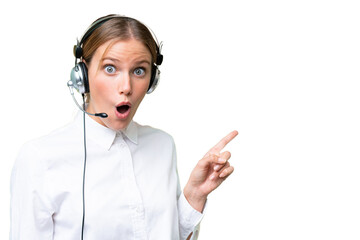 Wall Mural - Telemarketer caucasian woman working with a headset over isolated background surprised and pointing side