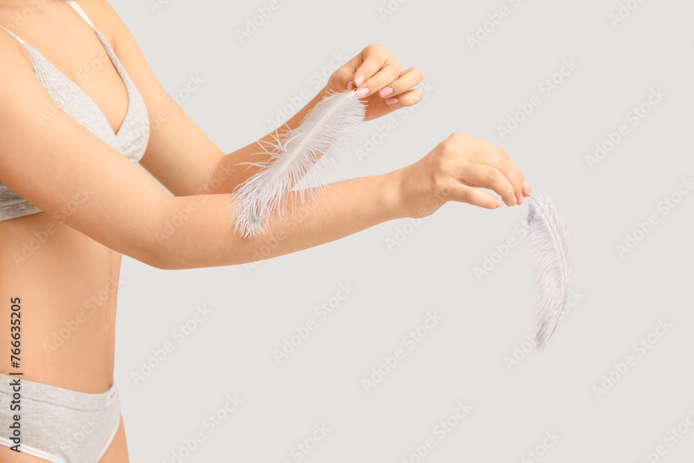 Young woman with soft feathers on grey background. Epilation concept