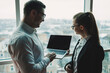 © Дмитрий Ткачук - A man and a woman are standing in the office against the background of a large panoramic window. Modern spacious workspace with employees. Business partners