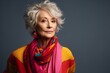 Portrait of a beautiful senior woman wearing colorful scarf over grey background.