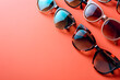 A series of stylish sunglasses in different shapes and colors arranged on a trendy coral background, epitomizing summer fashion