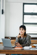 © Satori Studio - Confident young entrepreneur smiles while using her smartphone, surrounded by tech gadgets on her work desk in a bright office.