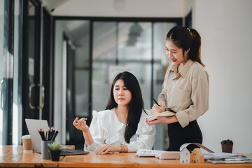 two professional women engaging in a collaborative work discussion with laptops and notes on a brigh