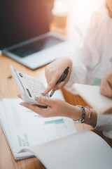 Close up of a business professional using a calculator for financial analysis over important documents with a laptop in the background.