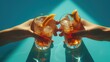 Two female hands holding glasses of whiskey with ice cubes and orange slices on the blue background