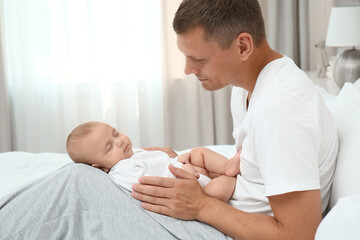 Wall Mural - Happy father holding his cute sleeping baby on bed at home