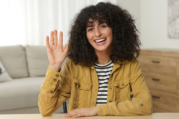 Happy woman waving hello at wooden table in room