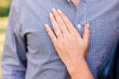 A man and woman standing together. She's got her hand with engagement ring on his shirt. 