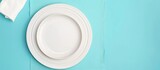 Fototapeta  - White plate and cotton napkin placed on a blue background. Ideal setting for a food-themed menu or recipe book, featuring a top-down view.