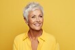 Happy senior woman smiling and looking at camera isolated over yellow background.