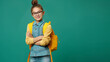 Full length portrait Schoolgirl in glasses with yellow backpack holding hands crossed while smiling happy on green background professional photography.