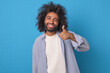 Young smiling Arabian man student shows thumbs up and winks giving positive feedback about watching movie from streaming service dressed in casual style stands on isolated blue background.