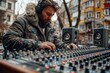 Focused male audio engineer in headphones using sound mixer on city street.
