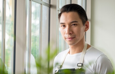 Portrait garden farm young asian man handsome one person stand smile fresh happy enjoy with bright smile look hand holding pot small tree leaf green plant in room work shop job hobby summer day relax