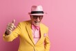 Cheerful senior man with hat and glasses showing thumb up on pink background