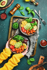 Sticker - Hands in a yellow sweater hold a bowl of salad: pumpkin, avocado, corn and tomatoes, clean eating concept. Top view