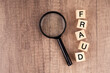 Fraud word on wood block and magnifying glass