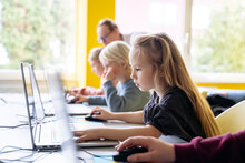 Blond girl using laptop learning computer programming in classroom