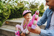 © Westend61 - Cheerful girl assisted by father in wearing roller skates sitting on steps