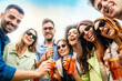 Laughing group of friends toasting with cocktails - celebrating friendship, summer joy, carefree outdoor fun - young adults with drinks in plastic glasses - copy space in the sky
