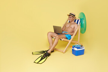 Wall Mural - tourist asian man working in laptop on deckchair isolated on yellow background. Summer vacation sea rest sun tan concept