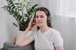 Carefree beautiful happy young woman sitting on cozy couch in headphones enjoy favorite music or listen audiobook, spend weekend time alone at home after hard work day. Time to relax, chill out